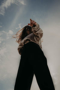 Woman with arms raised standing against sky