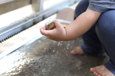 Baby hand holding wet cleaning brush while sitting barefoot on wet concrete floor