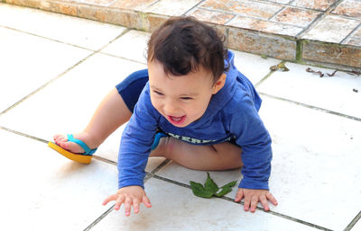 High angle view of cheerful baby boy sitting on tiled floor
