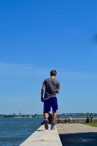 Rear view of man walking by sea against blue sky