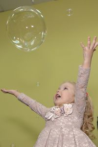 Low angle view of cute girl with arms outstretched looking at bubble against wall