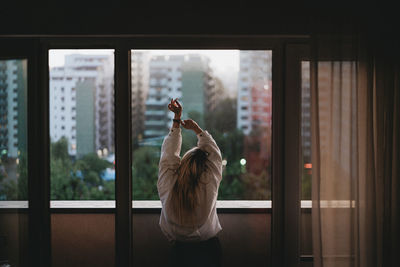 Rear view of woman standing by window at home