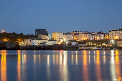 Illuminated buildings by sea against clear sky at night