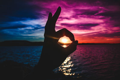 Close-up of silhouette hand against sea during sunset