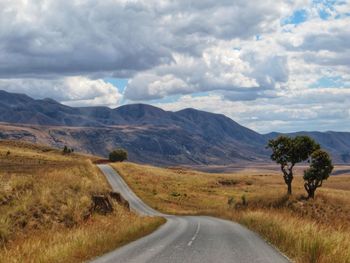 Country road on field against cloudy sky