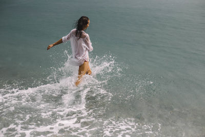 Rear view of woman splashing water in sea