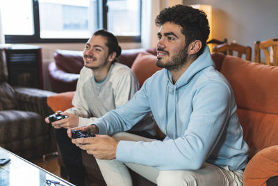 Male friends enjoying video game while sitting on sofa in living room