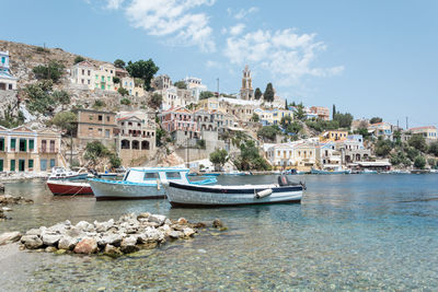 Sailboats moored in sea by townscape against sky