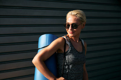 Sporty smiling blond woman in sportswear and sunglasses with yoga mat. workout outdoors. fitness