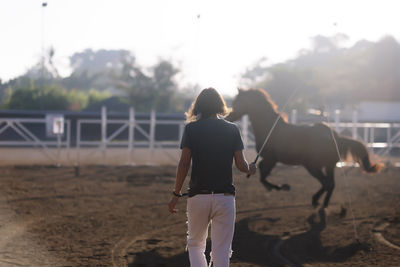 Rear view of woman training horse at ranch