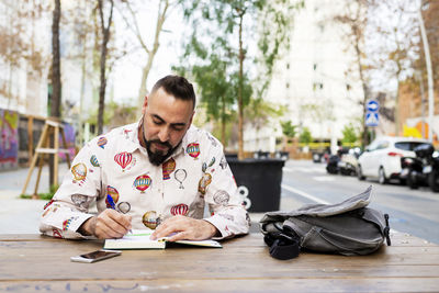 Bearded man sitting outdoors while working over a wooden table