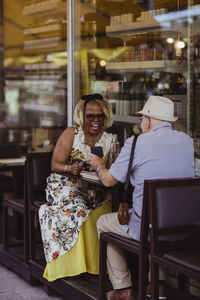 Senior woman laughing while man showing smart phone at sidewalk cafe