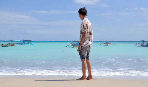 Rear view of woman standing at beach against sky