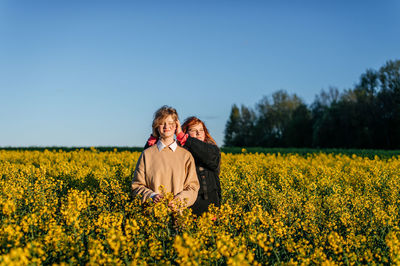 Rear view of woman standing amidst oilseed rape field against clear sky