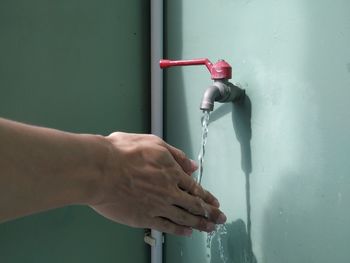 Close-up of hand holding faucet against wall