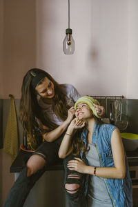 Smiling woman looking at friend wearing hat in kitchen