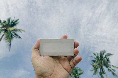 Cropped hand of man holding canvas frame against cloudy sky