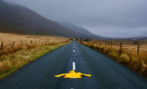 Raincoat on road amidst landscape against sky