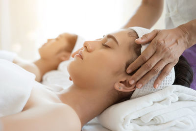 Cropped hands of massage therapist massaging young woman face in spa