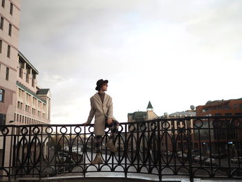 Rear view of man standing on railing against sky