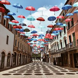 Multi colored umbrellas hanging amidst buildings in city