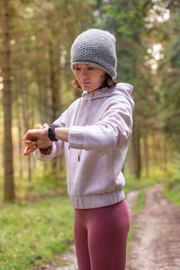Side view of focused female runner in sportswear checking pulse on fitness tracker during cardio workout in woods
