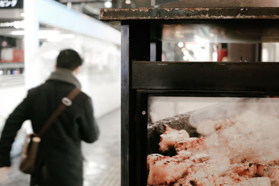 Close-up of meat in glass display with man walking in background
