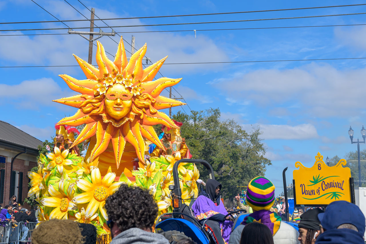 sky, group of people, carnival, tradition, celebration, architecture, festival, nature, city, cloud, event, day, men, crowd, outdoors, arts culture and entertainment, adult, headwear, large group of people, yellow, street, plant, building exterior, built structure, clothing
