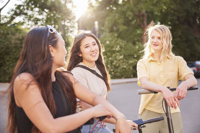 Young female friends spending time together outdoors riding electric scooters