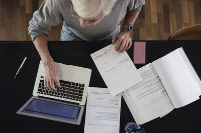 Directly above shot of senior man with bills using laptop at table