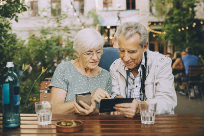 Senior couple using smart phone while sitting at restaurant in city