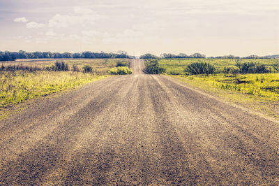 Dirt road amidst field against sky