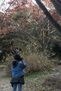 Rear view of a woman taking a photo during autumn