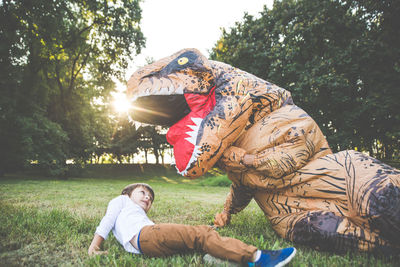 Boy playing with person wearing dinosaur costume in park