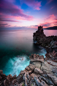 Rock formation on sea shore against sky during sunset