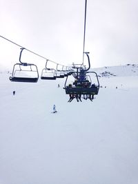 People sitting in ski lifts over snow covered field