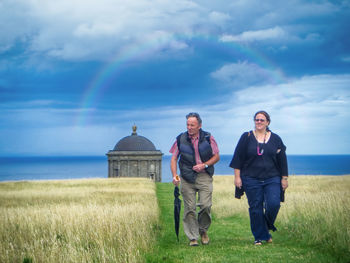 Full length of man and woman talking on grass against sky