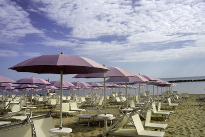 Deck chairs and parasols on beach against sky