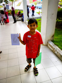 Portrait of boy holding drawing on paper while standing in school corridor