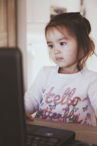 Cute girl looking away while using laptop on table