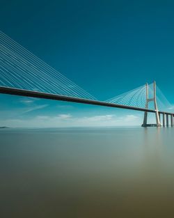 Suspension bridge over sea against blue sky