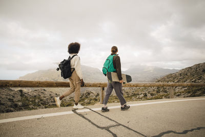 Young male and female friends looking at mountains while walking on road during vacation