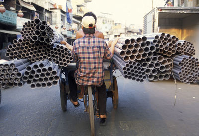 Rear view of people in tricycle while carrying pipes on street