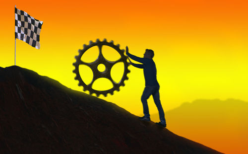 Silhouette men standing on rock against sky during sunset