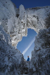 Portrait of young man standing by snow covered rock against sky