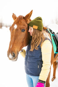 Smiling young woman standing by horse on snow covered field at winter