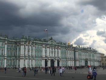 Tourists at town square against cloudy sky