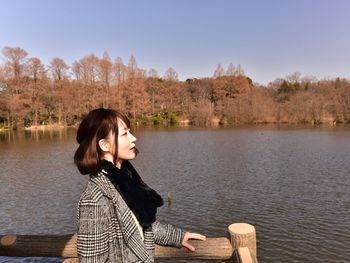 Young woman sitting by lake against sky