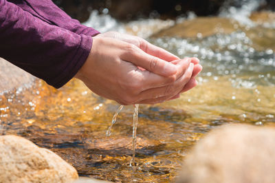 Person takes clean water from a stream in a forest or in the mountains. hand close up. sunny summer