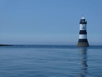 Lighthouse by sea against clear sky